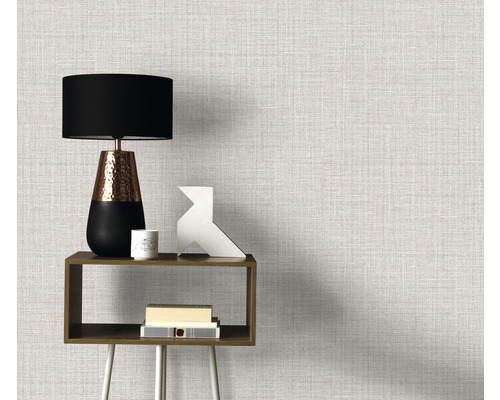 Prim-plan al unui perete cu tapet textil, o măsuță laterală, o lampă și obiecte decorative.