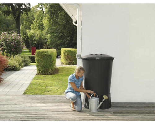 Femeie umplând o stropitoare la un butoi cu apă de ploaie în grădină