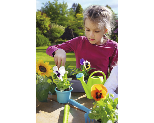 Fată plantează flori în grădină cu stropitoare și unelte de grădinărit