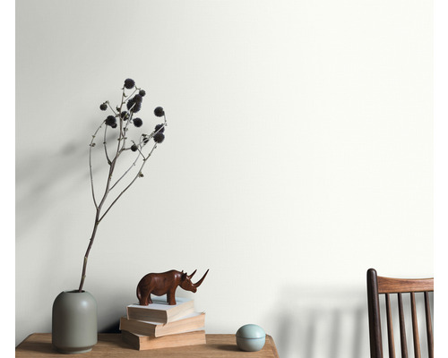 Cameră de zi cu aranjament de vază, obiect decorativ și stivă de cărți în fața unui perete vopsit.