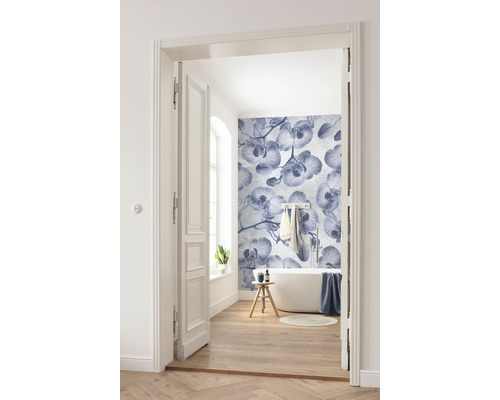 Baie luminoasă cu cadă, podea din lemn și fototapet cu model de orhidee, fotografiată printr-o ușă deschisă.