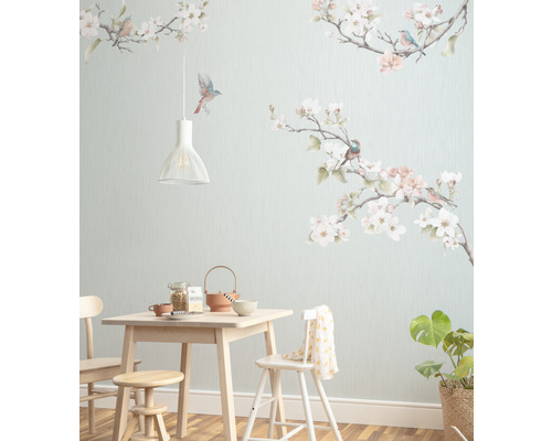 Sufragerie cu masă din lemn deschis, scaune, taburet, veselă, plantă de interior și tapet de perete cu motive de păsări și flori.