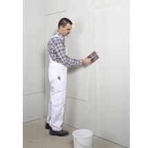 Muncitor aplică chit cu o spatulă pe un perete din gips-carton