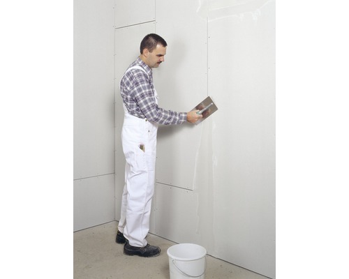 Muncitor aplică chit cu o spatulă pe un perete din gips-carton