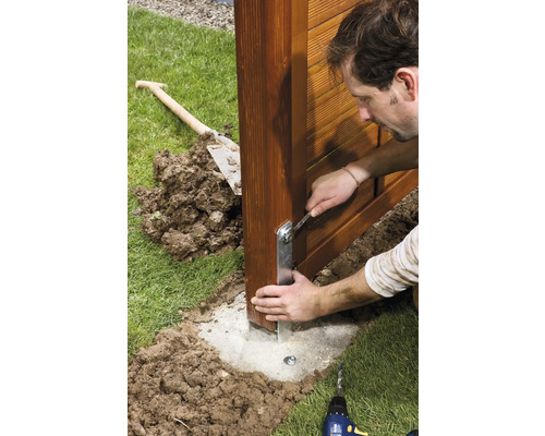 Bărbat montează stâlpul gardului cu o cheie pe o fundație de beton în grădină.