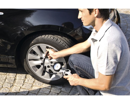 Bărbat verifică presiunea pneurilor la o mașină cu un manometru