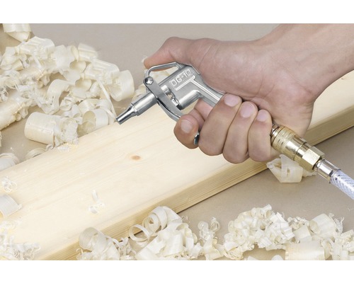 Pistol cu aer comprimat în mână lângă o scândură de lemn și așchii de lemn