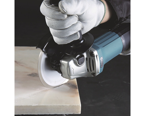 Un polizor unghiular cu disc diamantat taie o piatră, protejat de o mănușă.