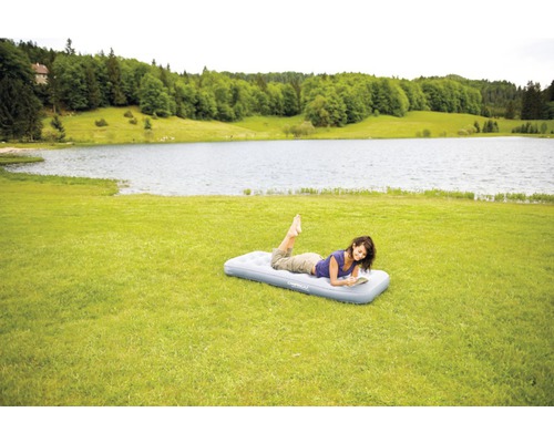 Femeie citind o carte pe o saltea pneumatică în verdeață cu un lac în fundal