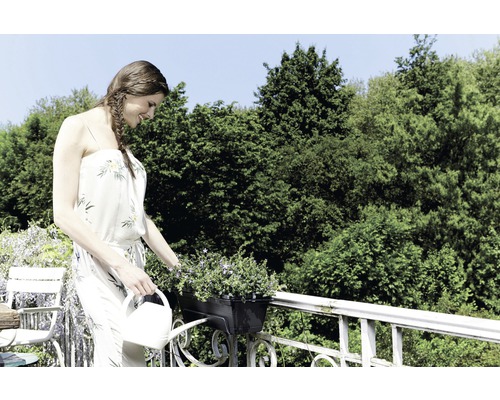 Femeie udând flori într-o jardinieră cu o stropitoare.