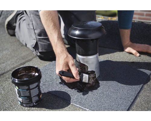 Artizanul etanșează o trecere de acoperiș cu o pensulă și material de etanșare.