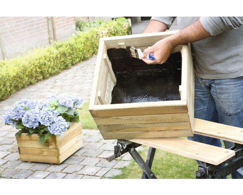 "Un bărbat vopsește un jardiniere de lemn cu o pensulă