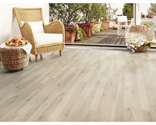 Pardoseală deschisă la culoare din lemn, cu fotoliu din răchită, fructe și flori pe terasă