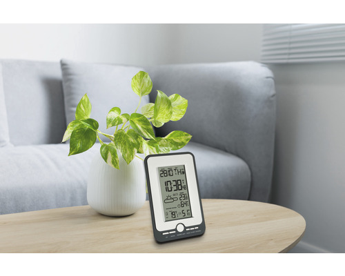 Stație meteo pe o masă cu plantă și canapea în fundal