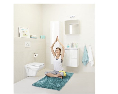 Baie luminoasă cu toaletă, chiuvetă, oglindă și o femeie care face yoga pe un covor