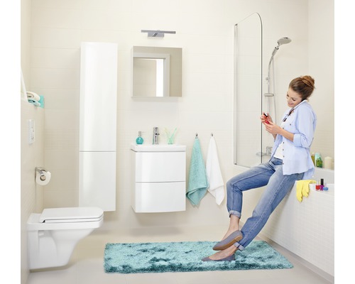 Baie cu toaletă, chiuvetă, oglindă, cadă și o femeie stând pe marginea căzii