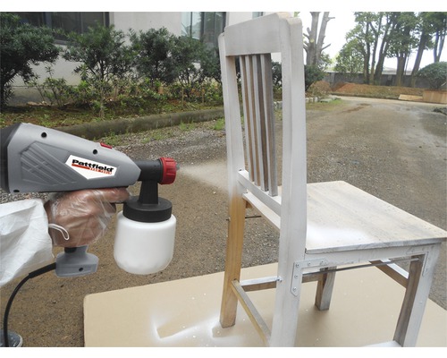 Pistol de pulverizare a vopselei pulverizând un scaun din lemn