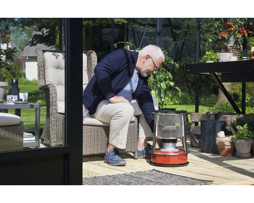 Un bărbat operează un încălzitor cu petrol într-o seră luminoasă cu mobilier și plante.