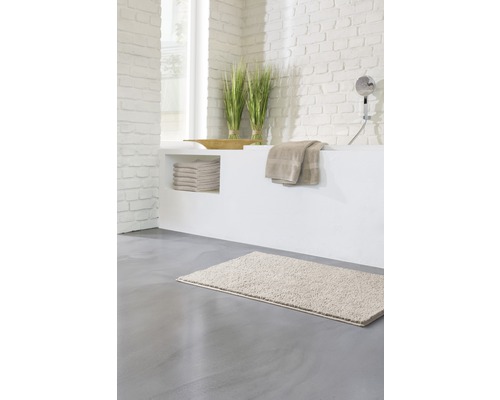 Baie luminoasă cu covoraș de baie, prosoape și decorațiuni pe o cadă zidită.