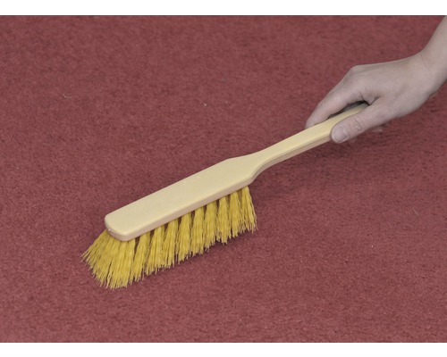 Mână ține o perie de curățare pe un covor