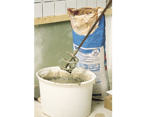 Mortar amestecat cu un mixer într-o găleată, un sac de mortar în fundal