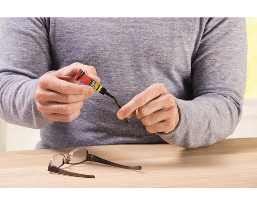 O persoană repară ochelari cu adeziv.