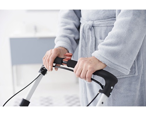 Prim-plan cu o persoană în halat care folosește un cadru de mers.