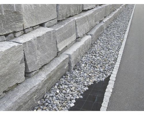 Un zid de sprijin din blocuri de granit gri, cu un strat de pietriș.