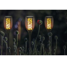 Trei lămpi solare în formă de torțe în grădină, printre plante cu flori.