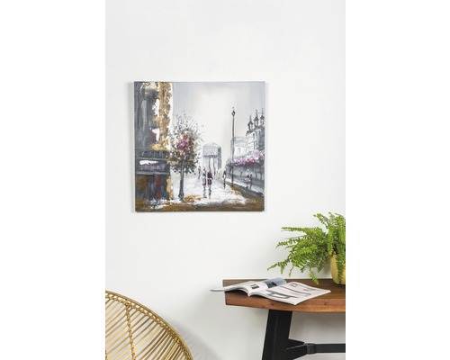 Tablou cu motiv urban pe perete deasupra unei mese cu reviste și o plantă.