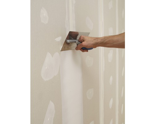 Un meșter tencuie un perete de gips-carton cu o spatulă.