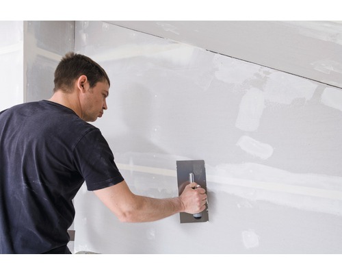 Un bărbat chituiește un perete din gips-carton cu o spatulă