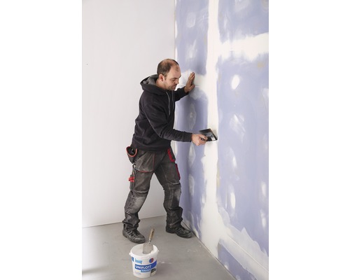 Bărbat care chituește un perete cu chit și cuțit de chit