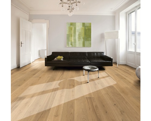 Cameră luminoasă cu podea din lemn, canapea, taburet și tablou