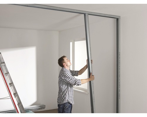 Bărbat care montează un perete de gips-carton cu profile metalice într-o cameră.