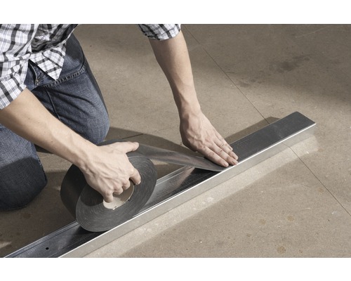 O persoană fixează bandă de etanșare pe un profil metalic.