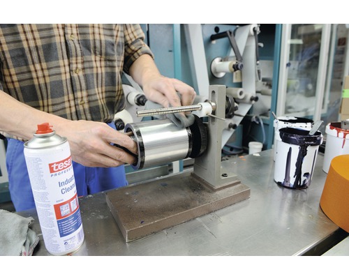 O persoană curăță un cilindru de imprimare cu un produs de curățare industrial Tesa.