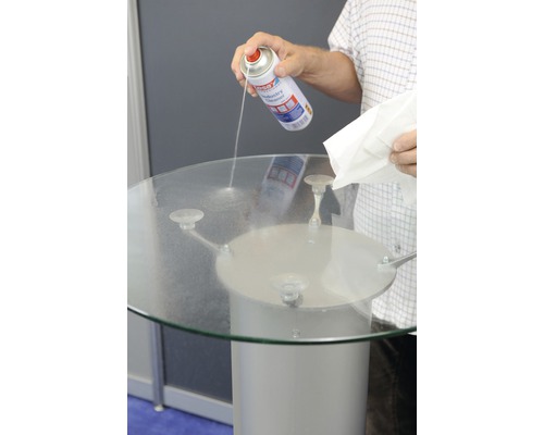 O persoană curăță o masă de sticlă cu un spray de curățare și o cârpă.