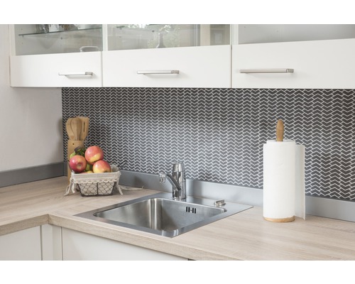 Chiuvetă de bucătărie din oțel inoxidabil cu robinet și ustensile de bucătărie pe un blat de lucru deschis la culoare în fața unui fundal întunecat cu model