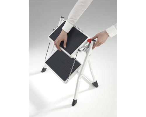 O persoană deschide o scară de uz casnic cu două trepte.