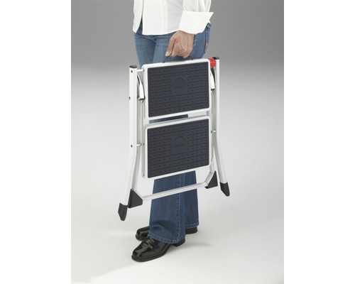 O persoană care transportă o scară pliabilă cu două trepte.