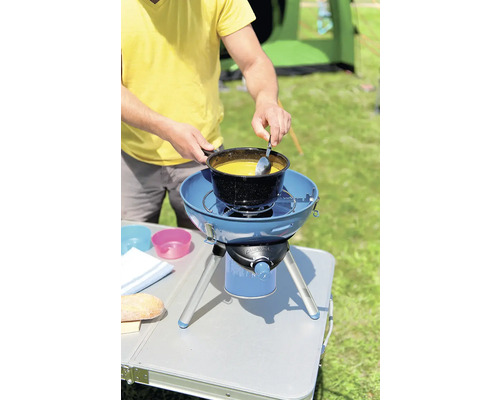 Bărbat gătește supă pe un aragaz de camping în aer liber.