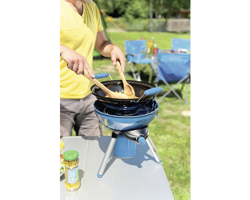 Persoană care gătește în aer liber cu un aragaz portabil pe gaz și un wok