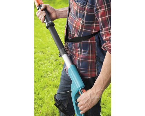 Un bărbat manevrează o foarfecă electrică de tuns gardul viu în grădină.