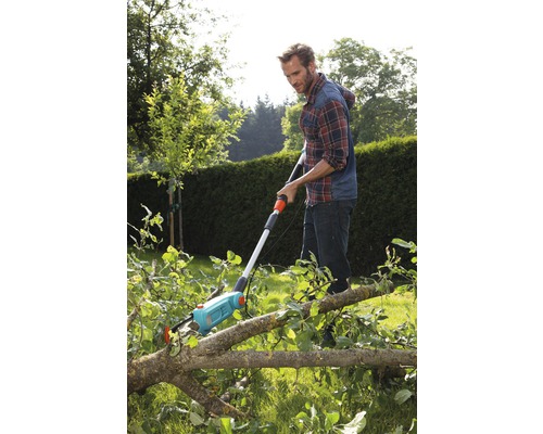 Un bărbat folosește un ferăstrău de crengi pentru a tăia crengi în grădină.