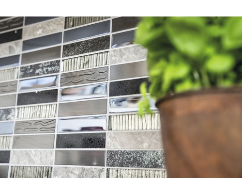 Prim-plan cu un perete cu plăci de mozaic în diferite nuanțe de gri, lângă o plantă