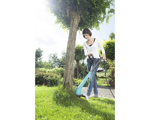 Femeie folosește o motocoasă în grădină pentru a tăia iarba.