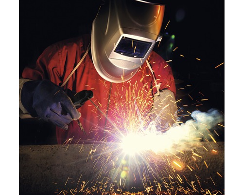 Sudor cu îmbrăcăminte de protecție și cască de sudură care sudează metal