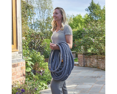 Femeie care poartă furtun de grădină flexibil din țesătură textilă în grădină