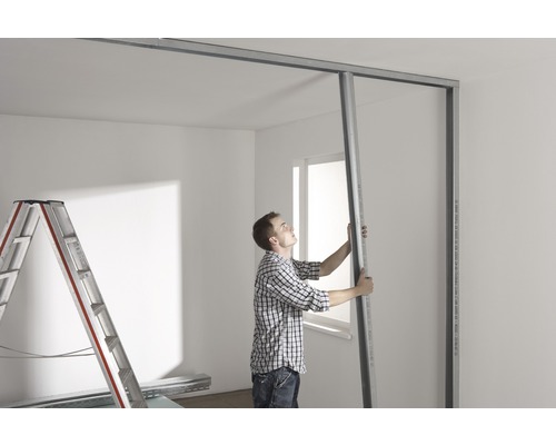 Bărbat care montează un perete de gips-carton într-o cameră luminoasă cu o scară